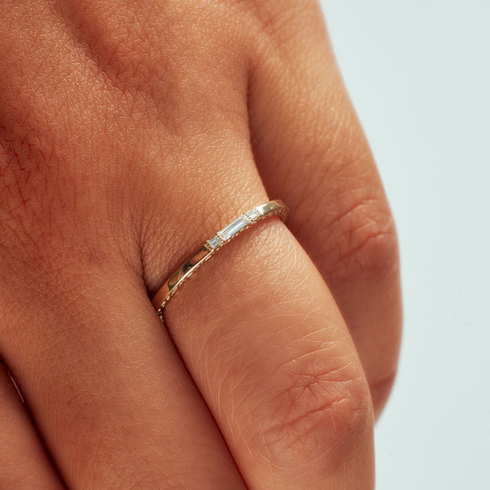 14k yellow gold band with textured side detail and baguette diamonds on hand model.