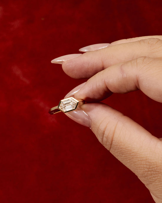close up of a hand holding the element 3 ring with an east west set hexagon diamond on red background
