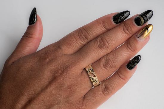 A model's hand wearing yellow gold cigar band with black and white diamonds